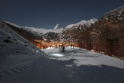 Piste in the dark with skiers looking down on the illuminated Zermatt, the Matterhorn in the background | © Gabriel_Perren