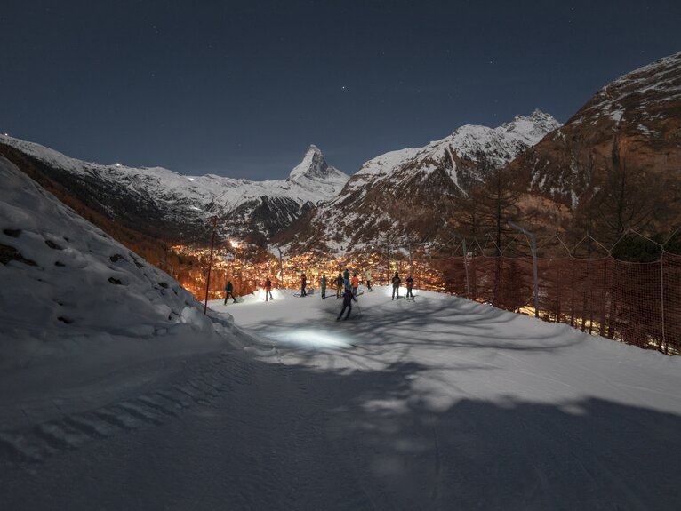 Piste in the dark with skiers looking down on the illuminated Zermatt, the Matterhorn in the background | © Gabriel_Perren