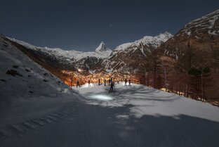 Piste in the dark with skiers looking down on the illuminated Zermatt, the Matterhorn in the background | © Gabriel_Perren