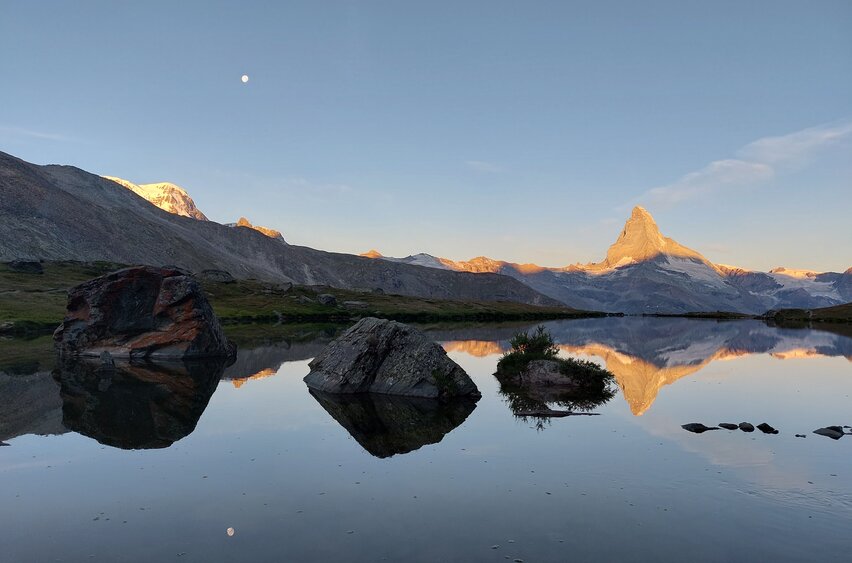 Le Cervin se reflète dans le lac Stelli. Les sommets qui entourent le Cervin sont également illuminés par les premiers rayons du soleil. | © Zermatt Bergbahnen