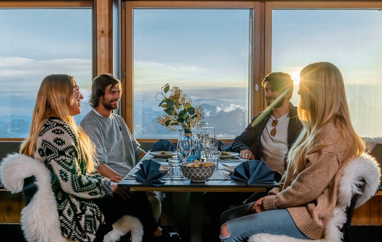 Due coppie sedute al tavolo del ristorante Glacier Paradise al tramonto | © basic home production