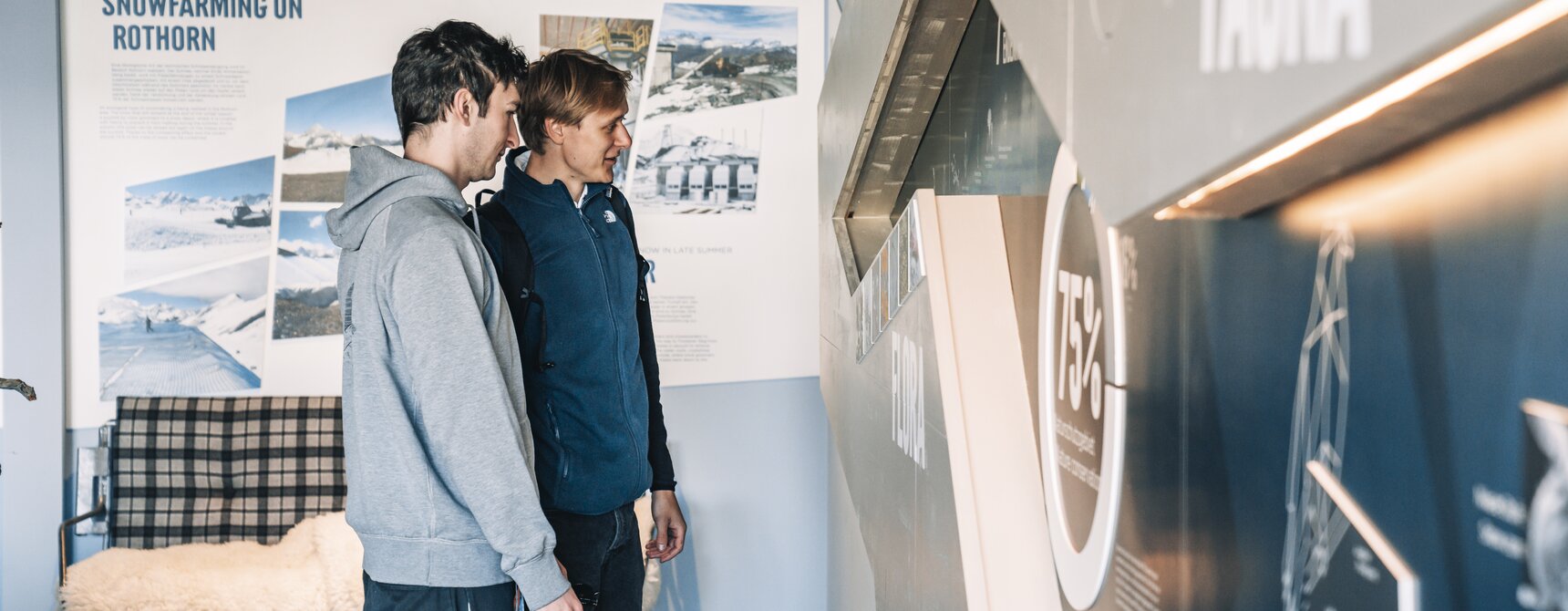 Zwei Männer betrachten die Informationstafeln in der Alpine Lounge auf Blauherd.  | © Gabriel Perren