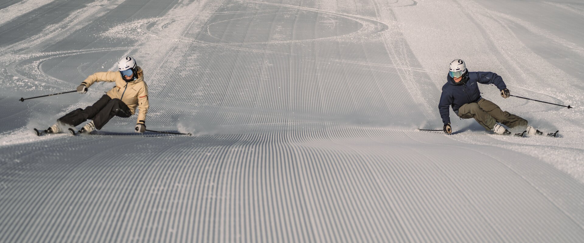 Two skiers make a turn on a freshly groomed slope. | © Gabriel Perren