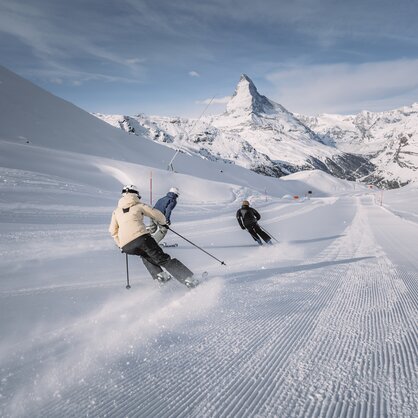 Three skiers skiing on freshly groomed slopes in the Matterhorn Ski Paradise. The Matterhorn can be seen in the foreground. | © Zermatt Bergbahnen
