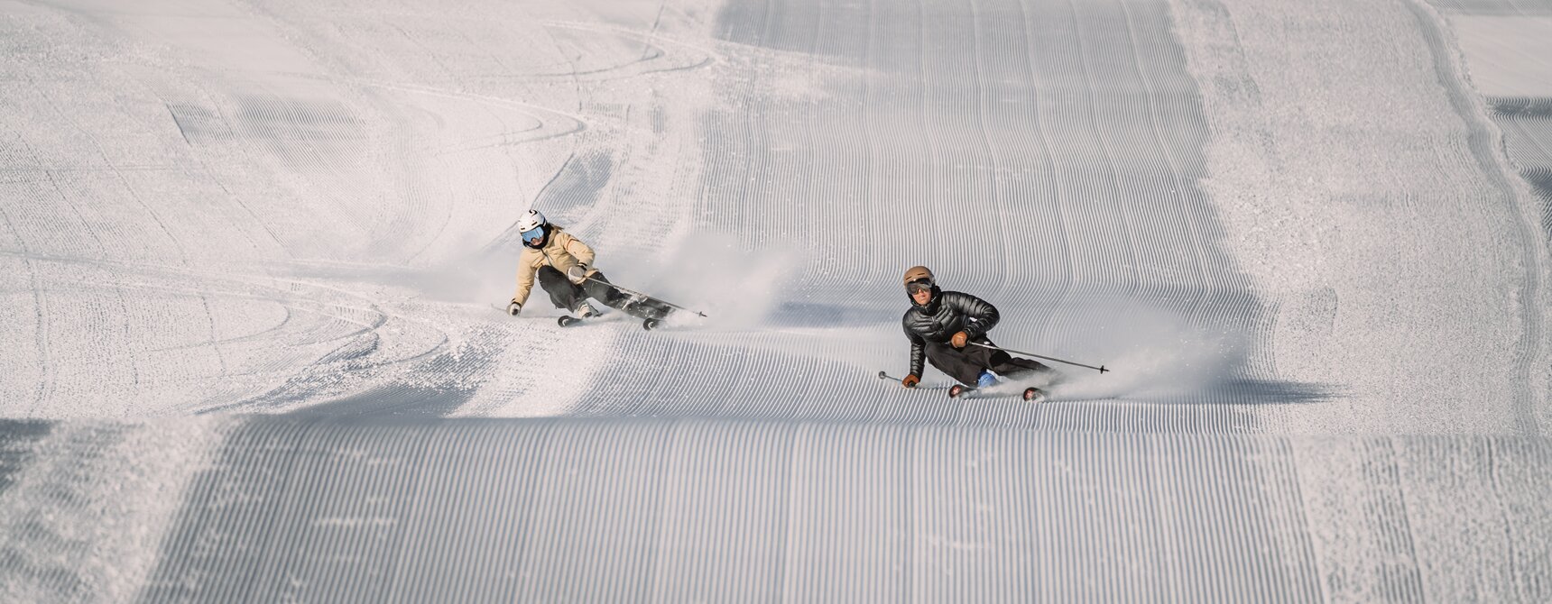 Zwei Skifahrer machen eine Rechtskurve auf frisch präparierten Skipiste.  | © Gabriel Perren