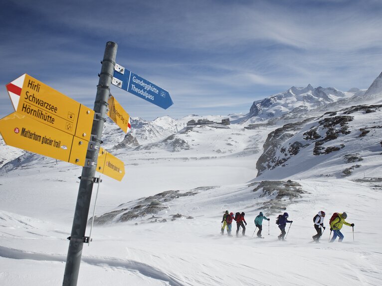 Group of snowshoers fighting their way through the snow, a signpost in the foreground | © Michi_Portmann