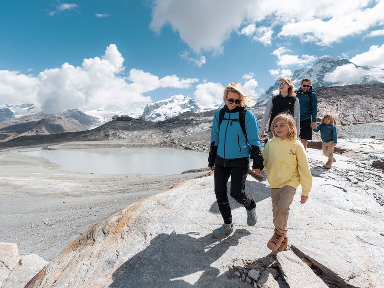 Familie mit drei Kindern wandert über Felsen, im Hintergrund die Zermatter Bergwelt | © basic_home