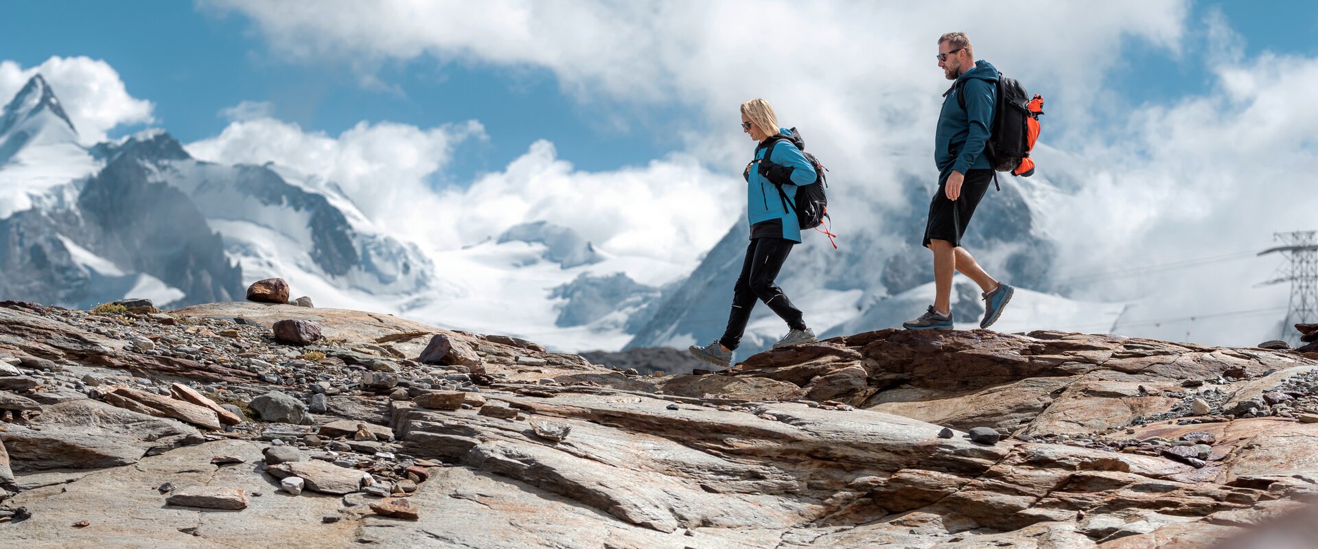 Zwei Personen wandern über Felsen, im Hintergrund die Zermatter Bergwelt | © basic_home