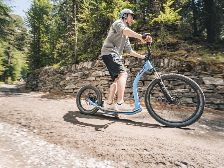 Un homme siffle en kickbike le long de la forêt.   | © Gabriel Perren