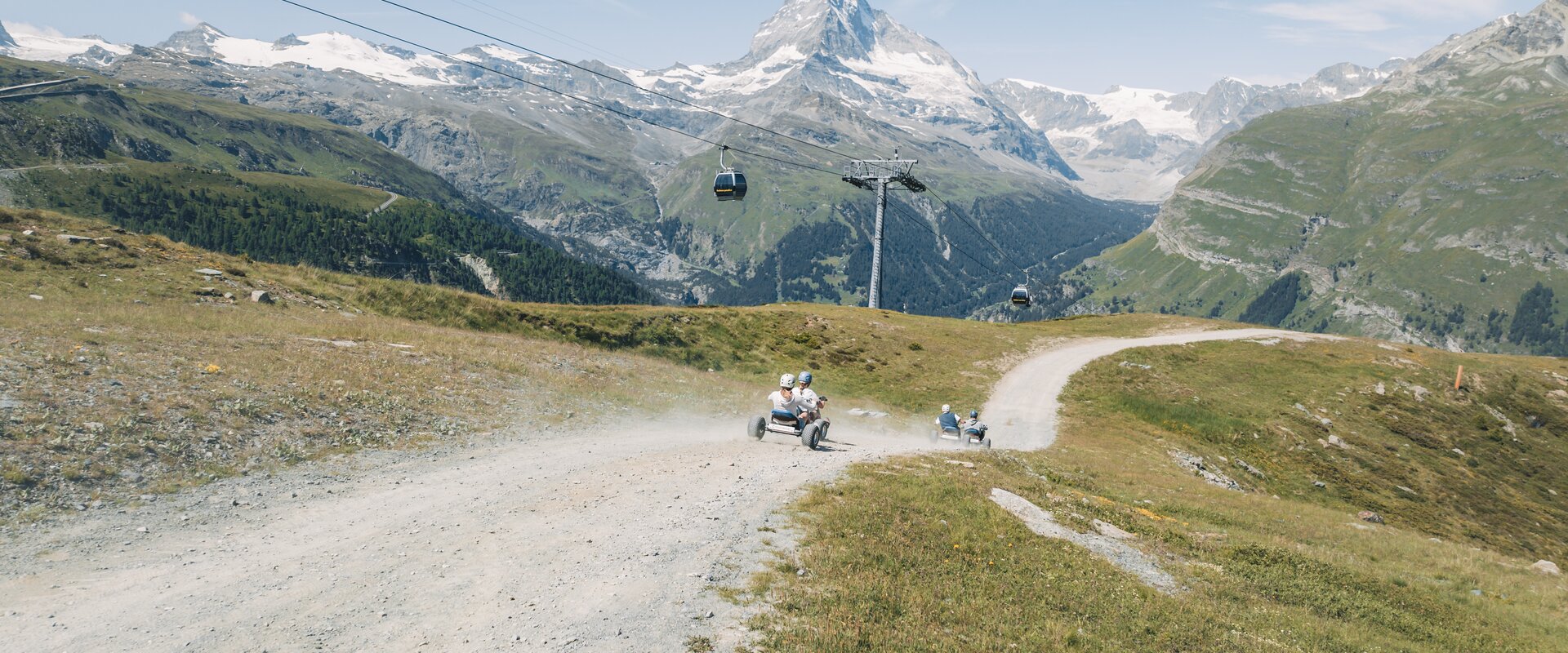Un gruppo scende dalla montagna con i mountaincarts sullo sfondo mozzafiato del Cervino.  | © Gabriel Perren