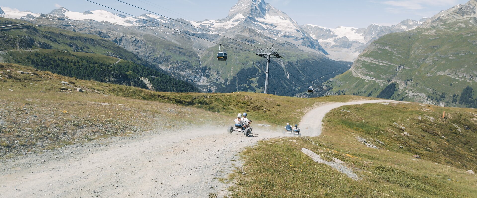 Eine Gruppe düst bei atemberaubender Kulisse des Matterhorns mit den Mountaincarts den Berg hinunter.  | © Gabriel Perren