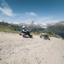 Deux hommes dévalent le chemin en mountaincarts avec le Cervin en arrière-plan. | © Gabriel Perren