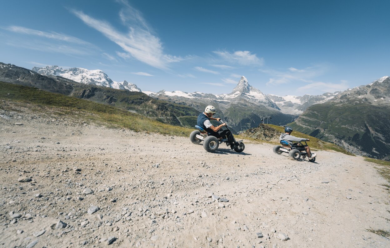 Two men hurtle down the path on mountain carts with the Matterhorn in the background. | © Gabriel Perren