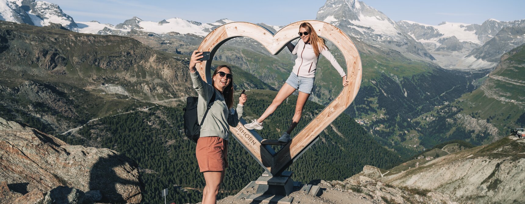 Two women take a selfie in front of the wooden heart on Blauherd.  | © Gabriel Perren